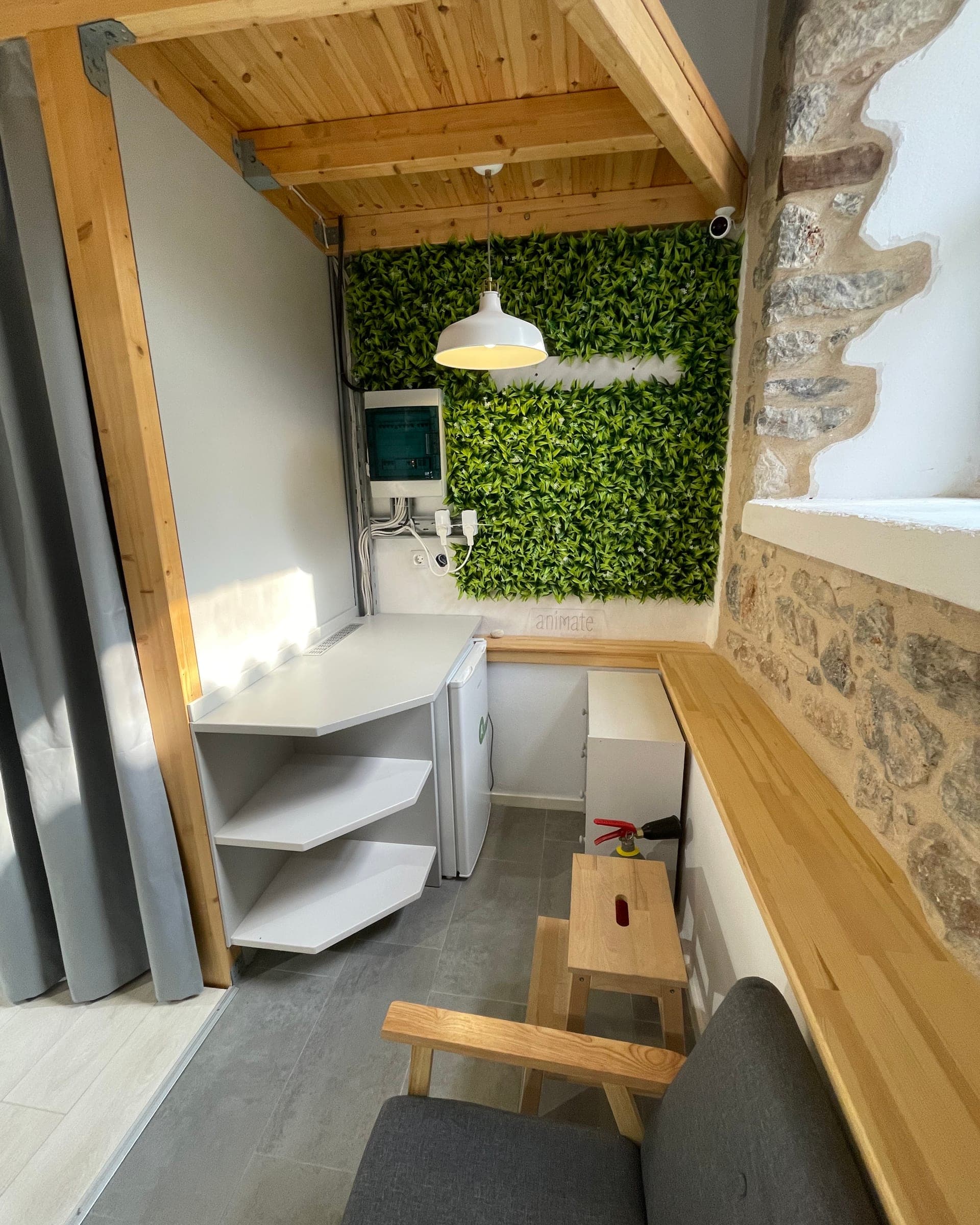 kitchenette corner with a fridge, shelves and a green plant wall under a wooden loft